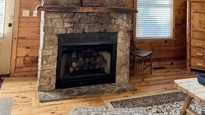 A log cabin interior with a stone fireplace, wooden walls, and large windows. - Cabin #1 - Fantasy Hideaway (Stanardsville)