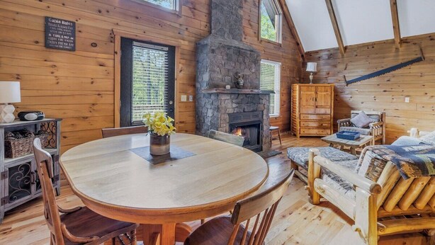 A wooden cabin interior with a stone fireplace, a round dining table, and a cozy seating area. - Cabin #1 - Fantasy Hideaway (Stanardsville)