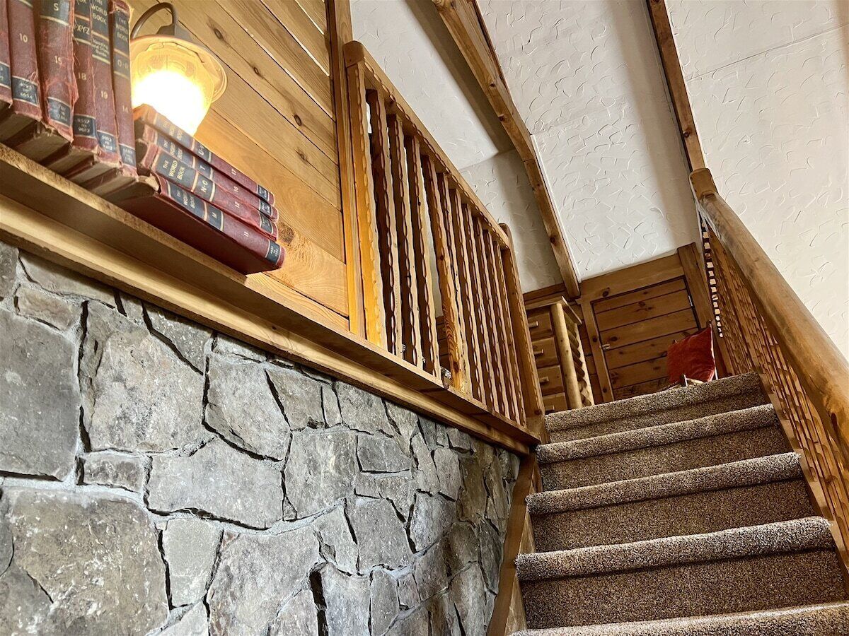 A stone wall, wooden staircase, and books on a shelf.