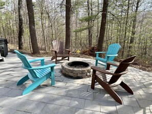 A fire pit surrounded by Adirondack chairs on a paved patio.