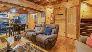 Accogliente interno di una baita in legno con divano, tavolo da pranzo, sedie e angolo cottura.