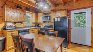 Cucina di una casetta in legno con tavolo, sedie, frigorifero, microonde, fornello e lavandino.