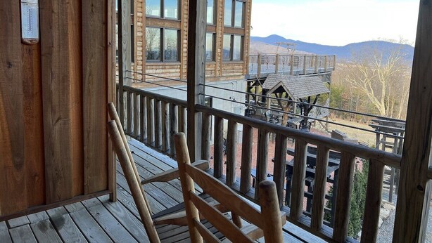 Un terrazzino in legno con una sedia di legno, un edificio in legno con diverse finestre e una vista sulle montagne sullo sfondo.