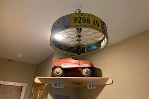 A ceiling fan with a circular light fixture and a vintage car model on a shelf below. - The Filling Station - Rm. 107 (Stanardsville)