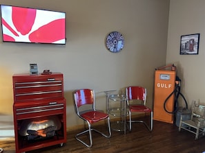 A room with a television, a clock, a gas pump, and two chairs.