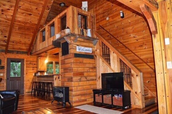 A wooden cabin interior with a staircase, a television, and a bar area.