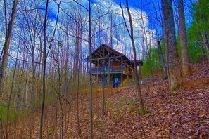 A cabin surrounded by trees with a wooden deck and a porch.