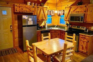 Interior de una cabaña de madera con cocina, mesa de comedor, sillas, refrigerador, microondas y estufa.