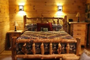 Una habitación tipo cabaña de madera con una cama, dos lámparas fijadas a la pared y un aparador de madera.