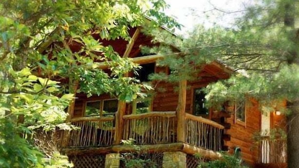 A rustic cabin with a wooden exterior, a balcony, and a surrounding forest. - Cabin #6 - Laurel Haven (Stanardsville)