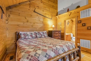 A wooden cabin interior with a bed, wooden walls, a window, and a door leading to a bathroom. - Cabin #6 - Laurel Haven (Stanardsville)