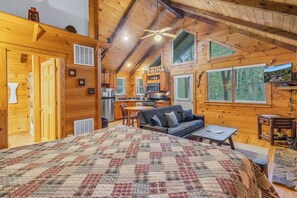 Un intérieur de chalet chaleureux comprenant un grand lit, un coin repas, une cuisine et un salon.