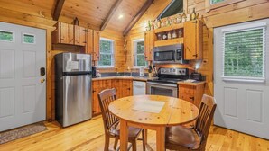 A wooden cabin interior with a kitchen, dining table, and chairs. - Cabin #6 - Laurel Haven (Stanardsville)