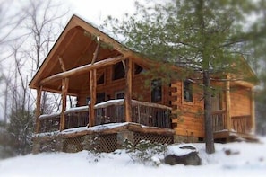 A log cabin with a porch, surrounded by snow and trees. - Cabin #6 - Laurel Haven (Stanardsville)