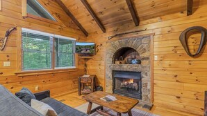A cozy cabin interior with a stone fireplace, wooden walls, a sofa, and a television. - Cabin #6 - Laurel Haven (Stanardsville)