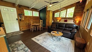A cabin interior with a wooden floor, a leather sofa, a dining table with chairs, and a ceiling fan. - Second Wind Mountain Cabin (Stanardsville)