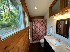 Un baño con detalles de madera, una ventana, cortina de ducha, inodoro, lavabo y espejo.