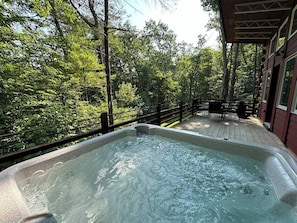 Un jacuzzi en una terraza de madera con vista a un bosque.