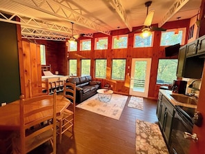 A wooden interior with a dining area, sofa, kitchen, and large windows. - Second Wind Mountain Cabin (Stanardsville)