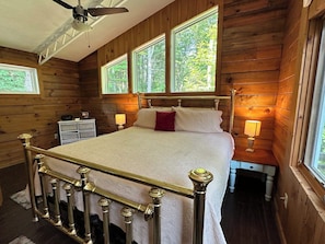 A wooden cabin bedroom with a bed, nightstands, a ceiling fan, and windows. - Second Wind Mountain Cabin (Stanardsville)