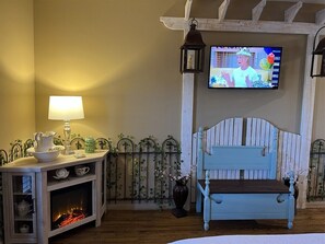 Une pièce confortable avec une télévision, une table avec une lampe, un banc et une cheminée.