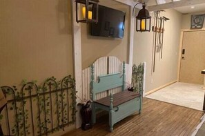 Une pièce avec un plancher en bois, un banc, un téléviseur fixé au mur et une porte.