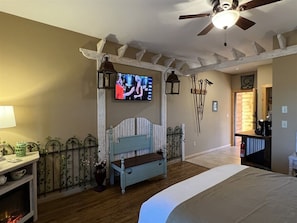 Quarto com cama, TV na parede, ventilador de teto e um banco de madeira.
