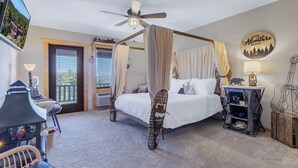 A four-poster bed with a canopy, a ceiling fan, a television, a desk with a lamp, and a wall clock. - Wild & Free Room. 202 (Stanardsville)