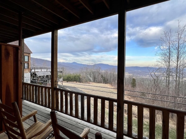 A wooden deck with a view of mountains and a train track.