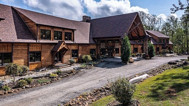 Un grand bâtiment de style chalet en bois, doté de nombreuses pièces, d’un porche couvert et d’une allée en gravier.