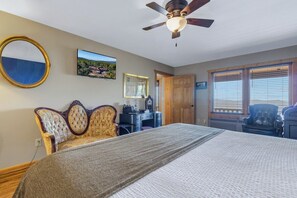 A bedroom with a bed, a ceiling fan, a desk, a chair, a mirror, and a window with blinds. - Presidential Suite - Rm. 205 (Stanardsville)