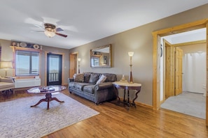 A living room with a leather sofa, a round coffee table, a ceiling fan, and a wooden door leading to another room.