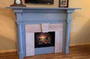 A fireplace with a clock above it, a framed picture on the wall, and a wooden floor. - Presidential Suite - Rm. 205 (Stanardsville)