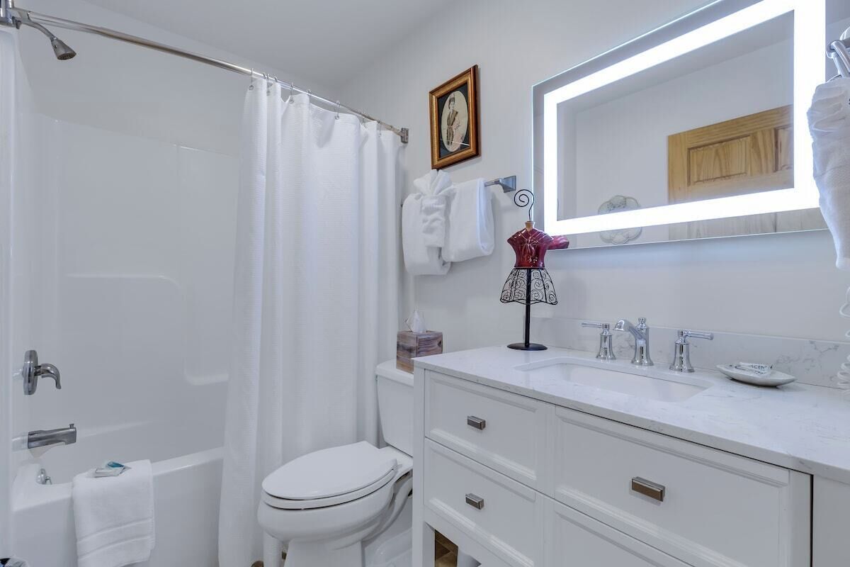 A bathroom with a bathtub, toilet, sink, and a mirror with lights.