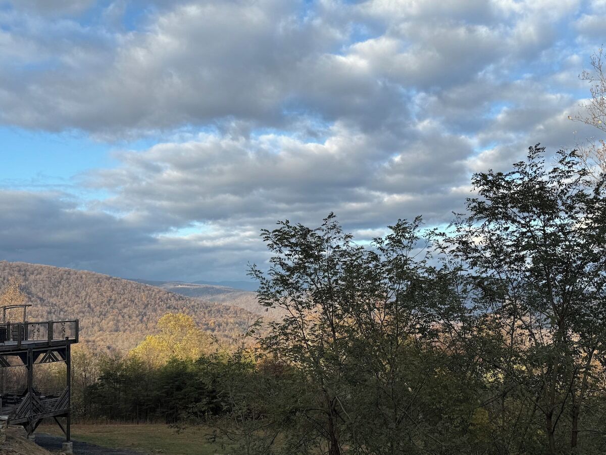 Une plateforme d’observation en bois surplombe une vallée boisée, avec une chaîne de montagnes visible au loin.