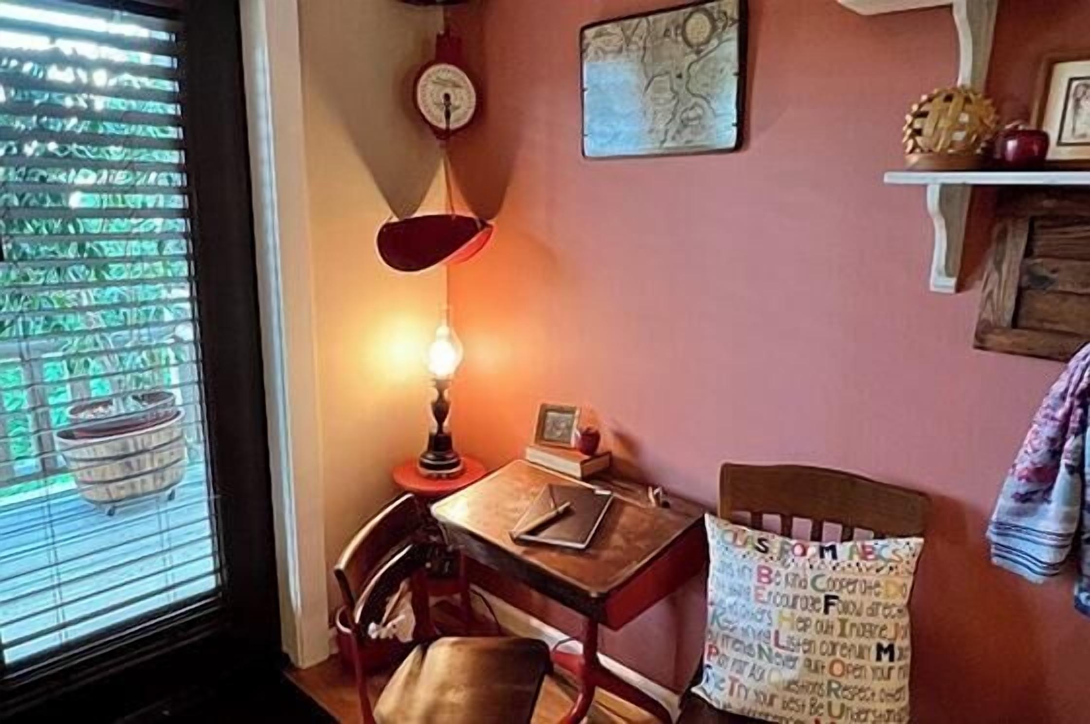 Ein Zimmer mit Schreibtisch, Stuhl, Lampe und einem Fenster mit Jalousien.