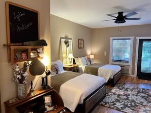 A bedroom with two beds, a ceiling fan, a chalkboard with a name, and a window with blinds. - Lydia Schoolhouse Rm. 112 (Stanardsville)