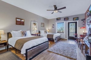 A bedroom with two beds, a ceiling fan, a desk with a chair, and a door leading outside. - Lydia Schoolhouse Rm. 112 (Stanardsville)