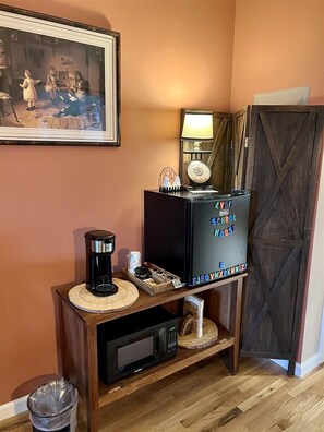 A room with a wooden console table, a coffee maker, a microwave, a framed painting, and a cabinet with a schoolhouse sign. - Lydia Schoolhouse Rm. 112 (Stanardsville)