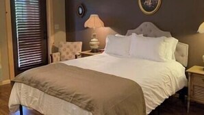 A bedroom with a bed, two bedside tables, a chair, and a lamp. - First Lady - Rm. 206 (Stanardsville)
