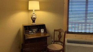 A corner room with a wooden dresser, a lamp, a chair, and a window with blinds. - First Lady - Rm. 206 (Stanardsville)