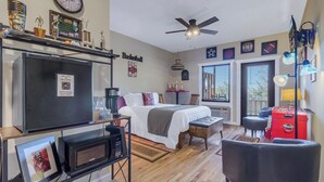 A compact room with a bed, a desk, a red chest of drawers, a ceiling fan, and a window with blinds. - Lydia Legends Rm. 111 (Stanardsville)
