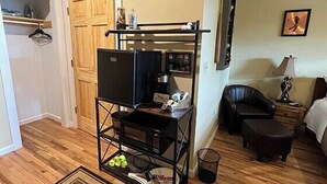 A compact living space with a kitchenette, a black sofa, a small table, and a clock on the wall. - Lydia Legends Rm. 111 (Stanardsville)