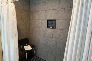 En duschhörna med kaklade väggar, en svart stol och en handduk på stolen.