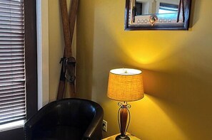 A room with a lamp on a table, a chair, a window with blinds, and a mirror on the wall. - Lydia Legends Rm. 111 (Stanardsville)