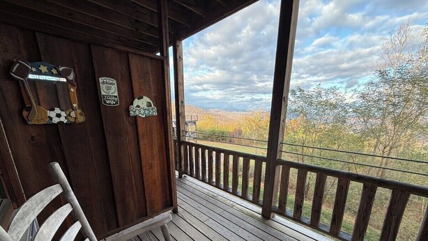A wooden porch with a railing, two rocking chairs, and a view of trees and hills. - Lydia Legends Rm. 111 (Stanardsville)