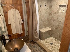 Un baño con un lavamanos grande, ducha con pared de azulejos y puerta de madera.