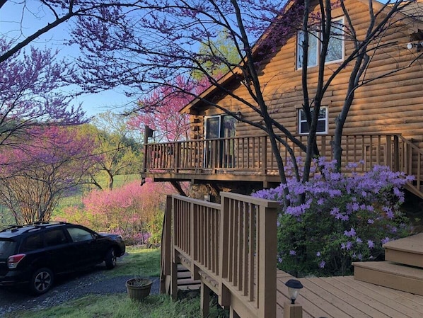 A wooden cabin with a deck and a car parked in front.