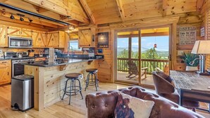 Interior de una cabaña con cocina, zona de bar y balcón con vistas.
