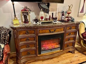 A wooden cabinet with a fireplace, drawers, and decorative items.